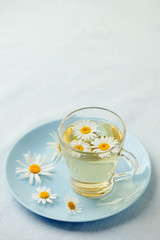 Herbal tea with fresh chamomile flowers in glass teacup on blue plate, seasonal colds flu alternative treatment, antidepressant and a remedy stomach cramps
