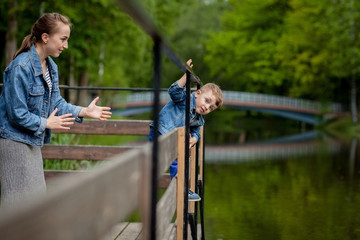 Mother is experiencing that the child will fall into the water. A little boy climbs a bridge railing in the park. The threat of drowning. Danger to children