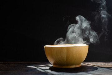Steam of hot soup with smoke wood bowl on dark background.selective focus