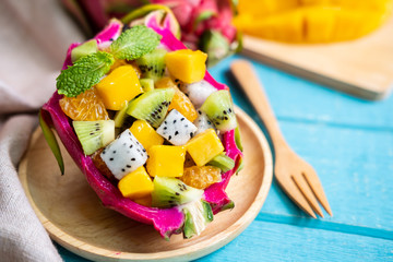 Mix tropical fruits salad served in half a dragon fruit on wooden table