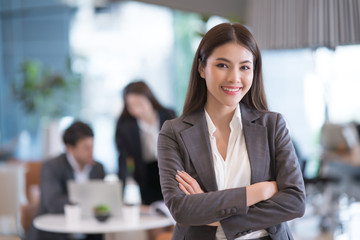 Portrait of successful young Asian businesswoman at office, colleagues in background.