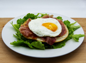 Fried egg with bread, ham, and salad on white dish, wooden table