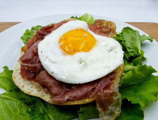 Fried egg with bread, ham, and salad on white dish, wooden table