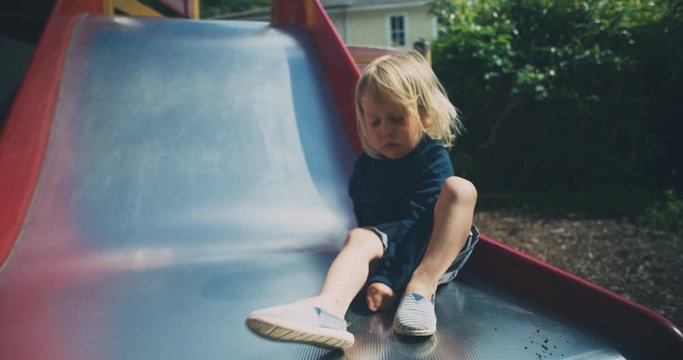 Little toddler sitting on a slide and putting on his shoe