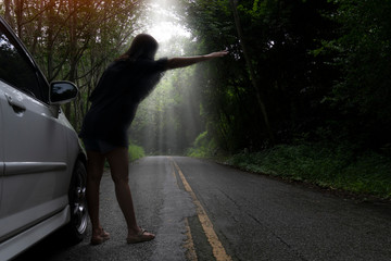 Women standing waving cars on the streets surrounded by dark forests. Beside the white cars on the asphalt road.