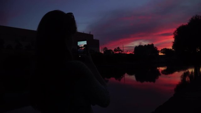 girl taking pictures of the sunset on a mobile phone camera.