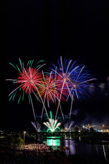 Imagen vertical de mucha gente observando los fuegos artificiales sobre el puente en el r&iacute;o con la ciudad vieja al lado