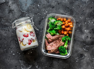 Balanced lunch box - breakfast - greek yogurt with strawberries and banana and lunch - steak, spicy chickpeas and broccoli on a dark background, top view