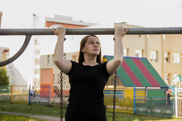 The girl is engaged in pulling up in the fresh air. . Use of the playground for sports