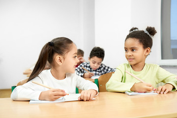 Cheerful classmates sitting at table in classroom at school