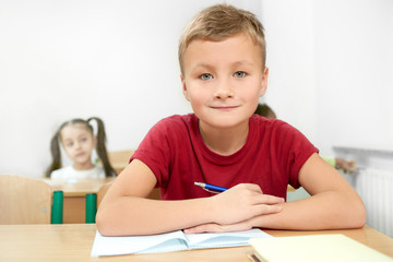 Fototapeta na wymiar Selective focus of cheerful boy sitting at desk in classroom