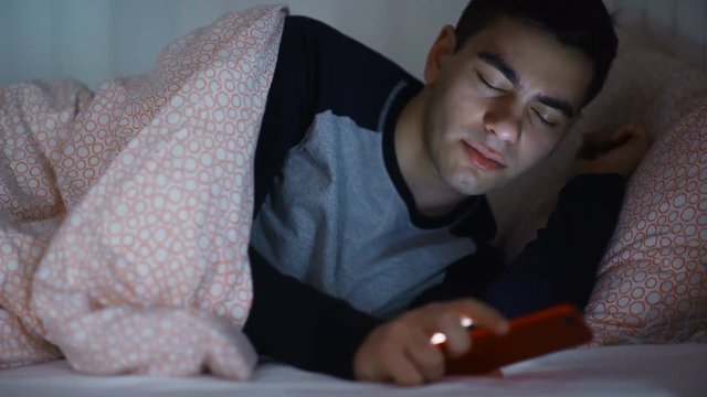 Man looking his smart phone in bed at night close up