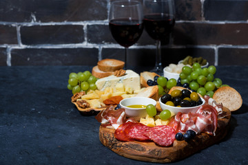 two glasses of red wine and assorted gourmet cheeses, fruit and meats