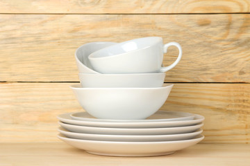 Piles of white ceramic tableware, plates, saucers and cups on a natural wooden background. kitchenware.