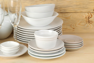 Fototapeta na wymiar Piles of white ceramic tableware, plates, saucers and cups on a natural wooden background. kitchenware.
