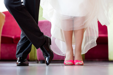 Legs of the groom in black shoes and trousers and brides in crimson heels with a snow-white hem of a wedding dress