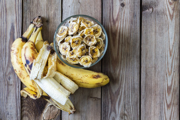 Ripe bananas with peeled peel and banana chips in a bowl on a natural wooden background. Copy space.