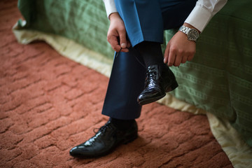 A man with a clock on his hands tying shoelaces on black shoes