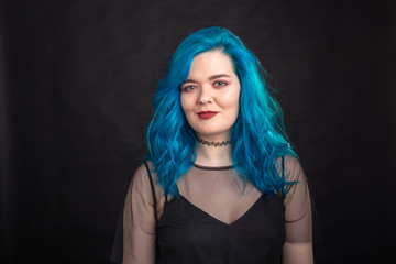 people, fashion and hair concept - close-up portrait of young woman in black dress with blue hair on black background