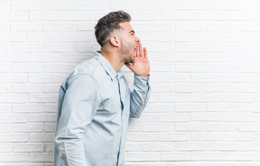 Young handsome man against a bricks wall shouting and holding palm near opened mouth.