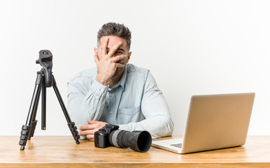 Young handsome photography teacher blink at the camera through fingers, embarrassed covering face.