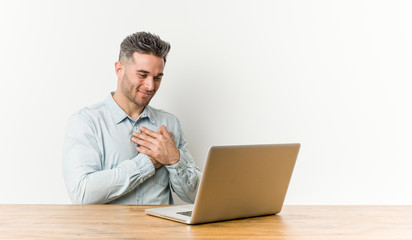 Young handsome man working with his laptop has friendly expression, pressing palm to chest. Love concept.