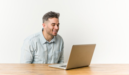 Young handsome man working with his laptop laughs and closes eyes, feels relaxed and happy.