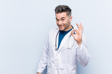 Young handsome doctor man cheerful and confident showing ok gesture.