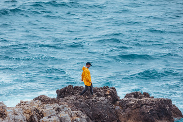 man walking by rock to storming sea