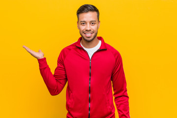 Young filipino fitness man showing a copy space on a palm and holding another hand on waist.