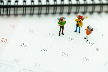 Miniature people: Tourists with backpacks standing on the travel calendar.