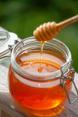 Pot Of Honey And Wooden Stick Are On A Table outdoors