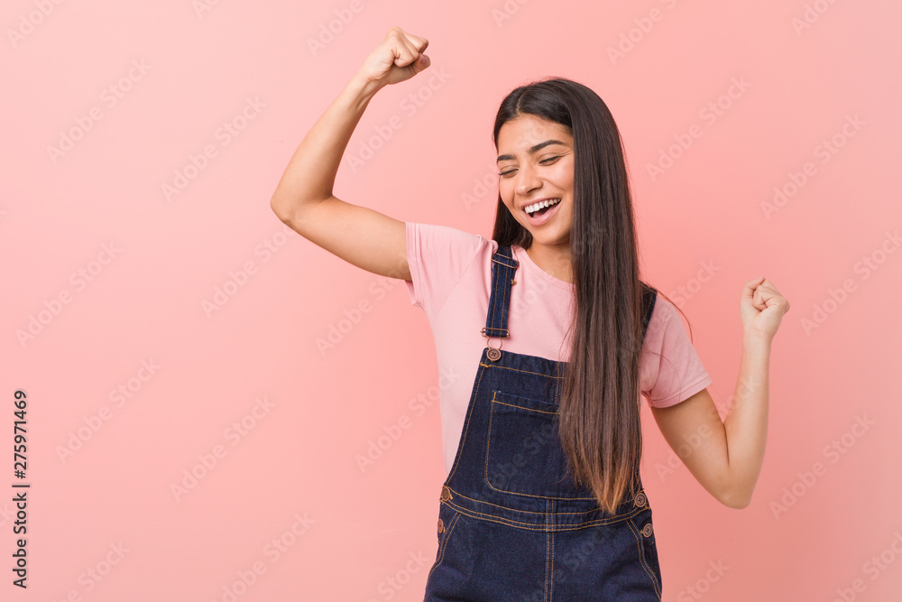 Wall mural Young pretty arab woman wearing a jeans dungaree raising fist after a victory, winner concept.