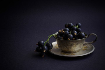 Black currant berries on a small metal plate and green stems on a black background