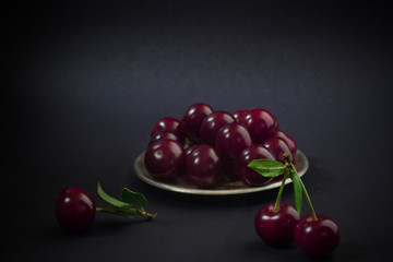 Cherry berries on a small metal plate and green stems on a black background