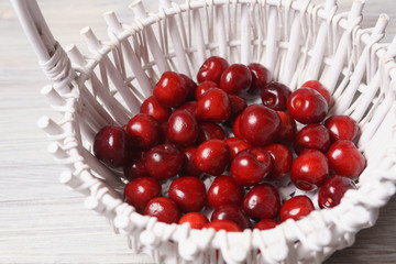 Red sweet cherries in a white basket on a white wooden table