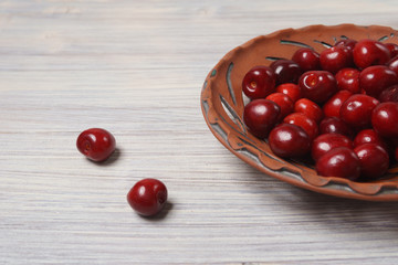 Red sweet cherries in a clay dish on a white wooden table