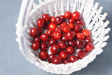 Red sweet cherry in a white basket on a gray background