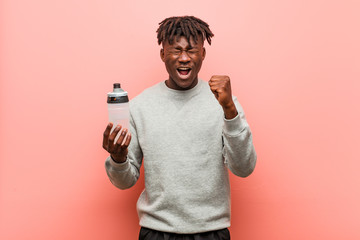 Young fitness black man holding a water bottle cheering carefree and excited. Victory concept.