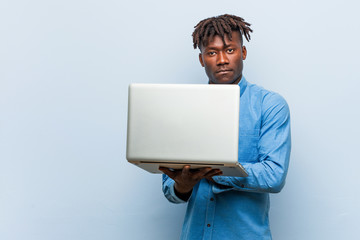 Young rasta black man holding a laptop smiling confident with crossed arms.
