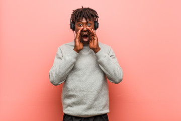 Young rasta black man listening to music with headphones shouting excited to front.