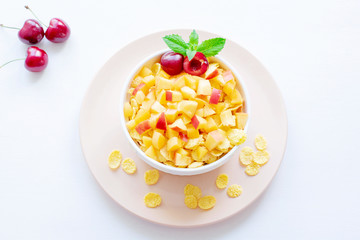 Healthy breakfast with cornflakes and pieces of fruit, cherries on a white background