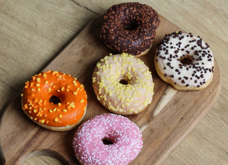 Different colorful donuts on wooden background. The are strawberry, banana, Chocolate, vanilla glazed flavor donuts. The donuts are decorated with different sprinles.