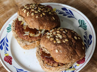 close up view of fresh tasty vegetarian soja hamburger on plate on wooden background. The burger has baked onions and curry ketchup