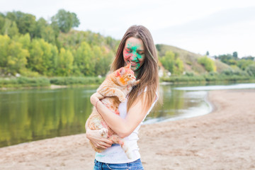 Festival holi, holidays, summer tourism and nature concept - young attractive young woman in paint with cat on natural background