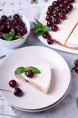 Piece of pie with sour cream and cherries topped with mint on the white plate