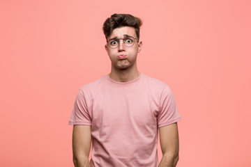 Young cool caucasian man blows cheeks, has tired expression. Facial expression concept.