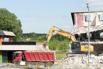 Yellow excavator loads construction debris into the truck. Technique destroys the building, is...