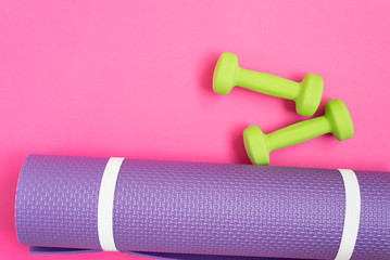 Yoga mat and dumbbells over pink background, top view. Sport concept