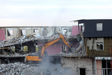 Excavator demolishes a residential high-rise building. The floors are broken, litter is lying around, dust is flying. The ruins of a house partially destroyed.